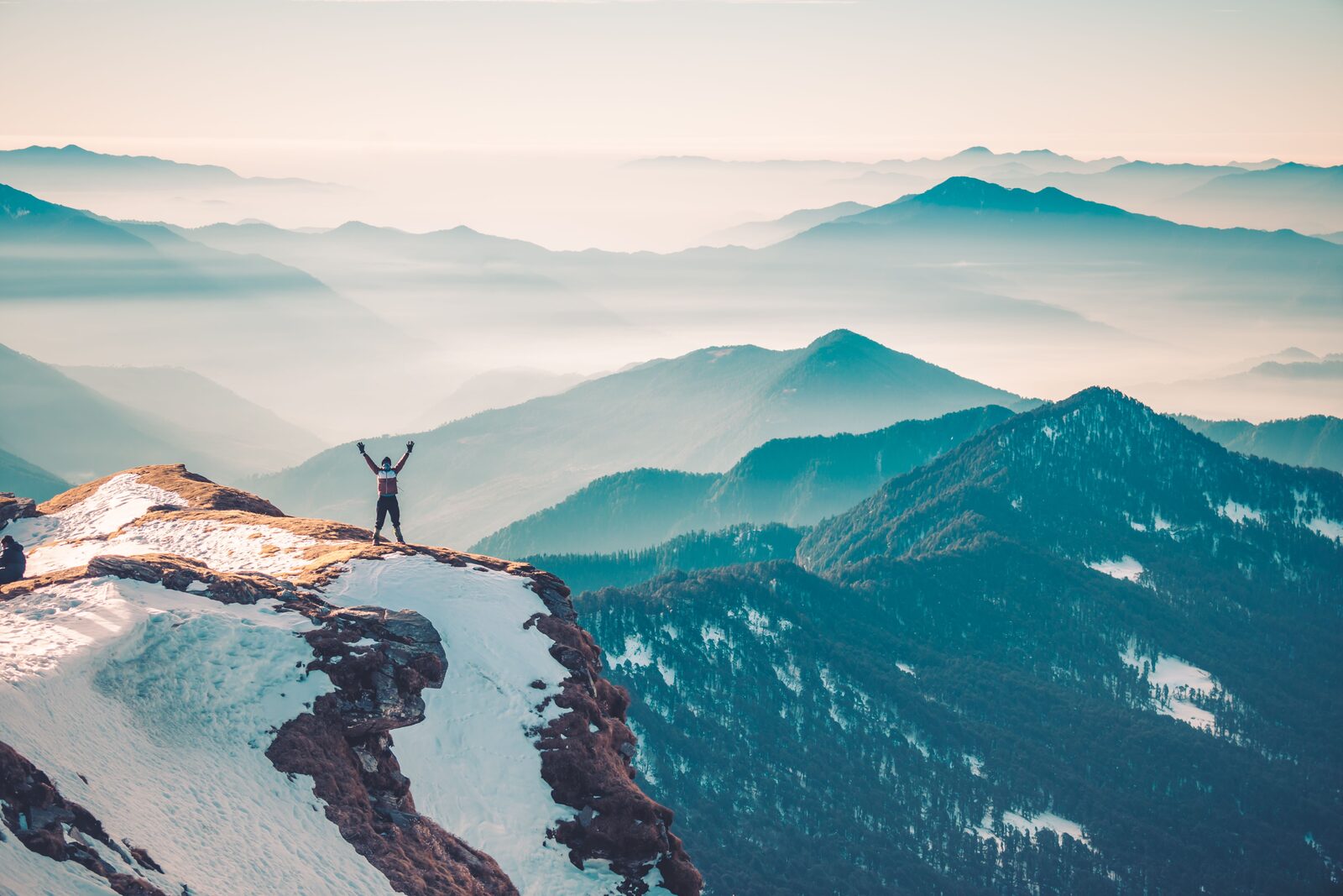 A lone figure standing on a snowy mountain summit above the clouds, arms raised